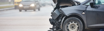 Acose up photo of a car crashed on a street with another care with headlights on in the background