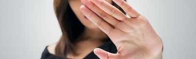A close up photo of a woman holding her hand up in front of her face signalling no 
